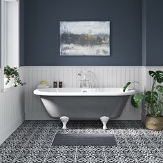 a white bath tub sitting next to a green plant in a blue and white bathroom