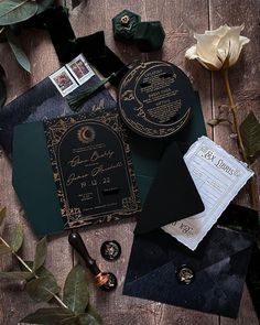 an assortment of black and gold wedding stationery on top of a wooden table with flowers