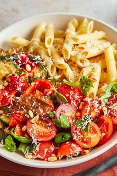 a white bowl filled with pasta, tomatoes and spinach on top of a red cloth