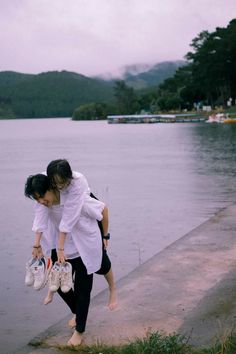 two people standing on the edge of a body of water with their arms around each other