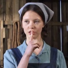 a woman wearing an apron and hat making a hand gesture with her finger in front of her mouth