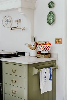 a kitchen with green cabinets and white counter tops, including a basket of fruit on the island