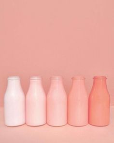 five different colored milk bottles lined up against a pink wall