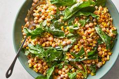 a bowl filled with corn and spinach on top of a white countertop next to a spoon