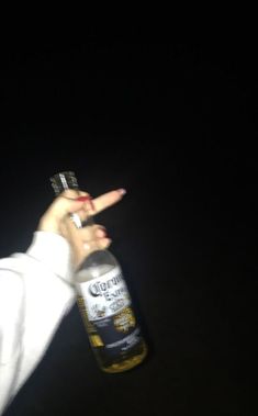 a person holding up a beer bottle in the dark with their finger pointing at it