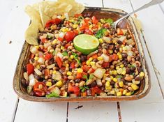 a dish filled with beans and corn next to a tortilla chips on the side