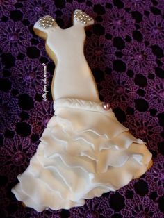 a wedding dress shaped cookie sitting on top of a purple doily covered tablecloth