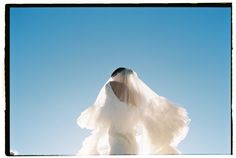 a woman in a wedding dress with her veil flying through the air on a sunny day