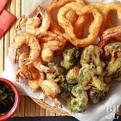 some fried vegetables and onion rings are on a basket next to a bowl of dipping sauce