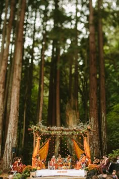 an outdoor ceremony in the woods with orange draping and yellow draped cloths