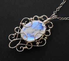 This stunningly elegant pendant necklace is handcrafted from sterling silver and a gorgeous rainbow moonstone cabochon, with lovely flashes of blue color. Pendant comes with an Italian made .925 sterling silver chain with lobster clasp (see photos) in your choice of length. Generously sized bail allows you to swap out different chain styles, if desired. One of a kind pendant measures approximately 2 inches long by 1.25 inches wide, and will come beautifully gift boxed, as shown in last photo. Sh Oval Moonstone Wire Wrapped Necklaces, Oval Moonstone Necklace Wire Wrapped, Handmade Moonstone Jewelry In White Gold, Handmade White Gold Moonstone Jewelry, Elegant Hand Forged Moonstone Jewelry, Oval Moonstone Wire Wrapped Jewelry, Wire Projects, Moonstone Pendant Necklace, Harpers Ferry