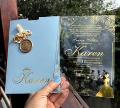 a person holding up a blue and gold wedding card with a brooch on it