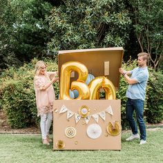 a man and woman standing in front of a cardboard box with the letters b is for balloon