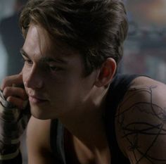 a young man with tattoos on his arm and shoulder holding a cell phone to his ear