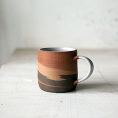 a hand holding a coffee cup on top of a wooden table with white walls in the background