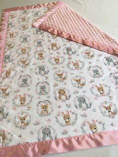 a baby blanket with dogs on it and pink trim around the edges, laying on top of a bed