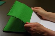 a person is cutting fabric on top of a piece of white paper with green felt