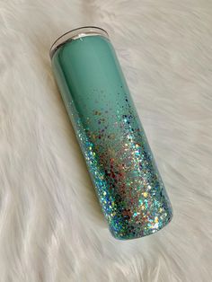 a green and blue glitter tumbler sitting on top of a white fur covered floor