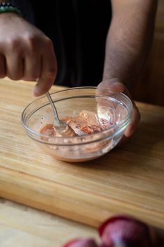 a person is stirring something in a bowl on a cutting board with apples around them