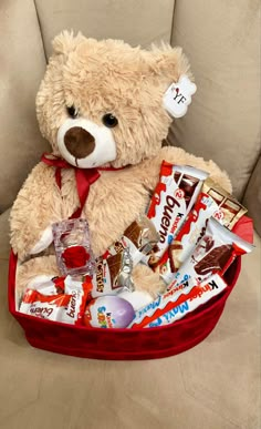 a teddy bear sitting in a red basket filled with candy and candies on a couch