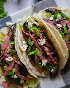 three tacos with meat, lettuce and red onions on a white plate