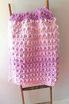 a pink and purple crocheted blanket sitting on top of a wooden chair next to a wall