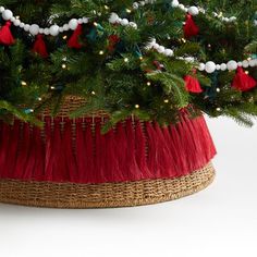 a christmas tree in a woven basket with red and white tassels on it