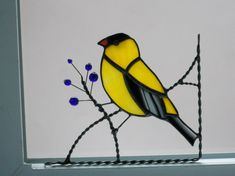 a stained glass yellow bird sitting on a branch with blue flowers in the foreground