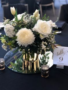 a vase with white flowers and greenery on a table at a wedding reception,