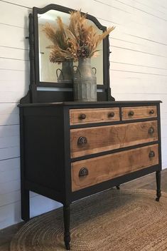 an old dresser has been painted black and is holding a vase with dried flowers on it