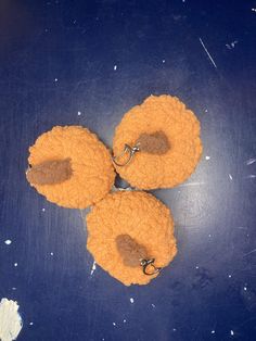 three orange donuts on a blue surface with two hooks attached to the doughnuts