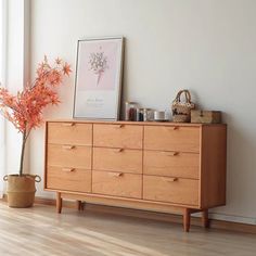 a wooden dresser sitting in front of a window next to a vase with flowers on it