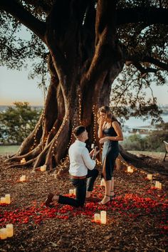 a man kneeling down next to a woman in front of a tree filled with candles