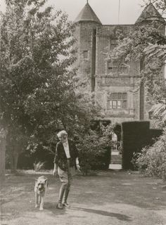 an old black and white photo of a man walking his dog in front of a house