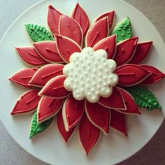 a decorated cookie on a white plate with green leaves and red flowers in the center