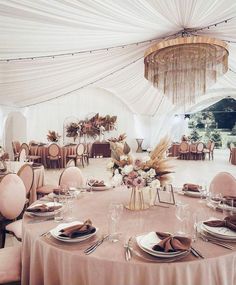 a banquet hall with tables and chairs covered in white drapes, chandeliers and pink linens