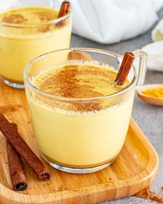 two glasses filled with cinnamon pudding on top of a wooden cutting board next to cinnamon sticks