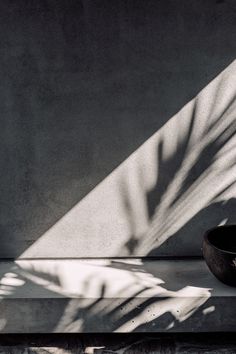 a black bowl sitting on top of a cement floor next to a shadow cast wall