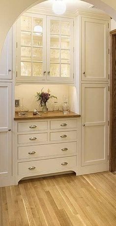 a kitchen with white cabinets and wood flooring in an archway leading to the dining room