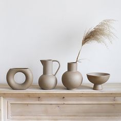 three vases sitting on top of a table next to a bowl and a plant