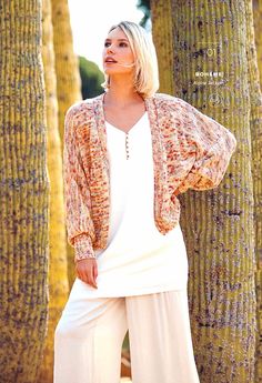 a woman standing in front of palm trees wearing white pants and a cardigan sweater