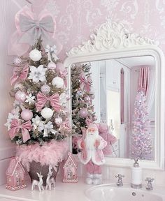 a pink christmas tree decorated with white and pink ornaments in front of a bathroom mirror