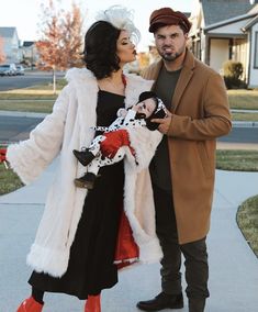 a man and woman dressed in costumes standing next to each other on a sidewalk with houses in the background