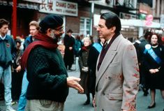 two men talking in front of a crowd of people on a street with blood all over them