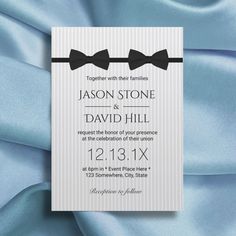 a wedding card with bow ties on it and blue satin fabric in the foreground