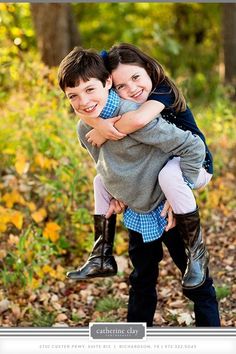 two young children hugging each other in the woods with autumn leaves around them and trees behind them