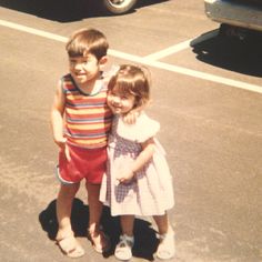 two young children standing next to each other on the street in front of a car