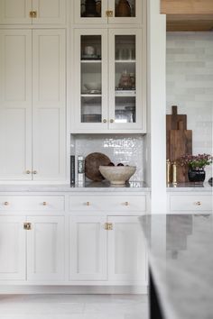 a kitchen with white cabinets and marble counter tops, including a bowl on the island