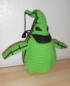 a crocheted green stuffed animal with black eyes and mouth, holding a string