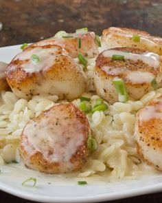 scallops and rice on a white plate with green onions in the center, sitting on a wooden table